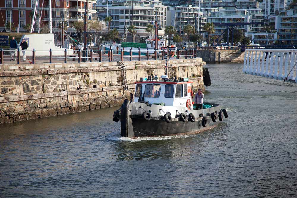 White and turquoise tugboat navigating Cape Town harbour waterfront