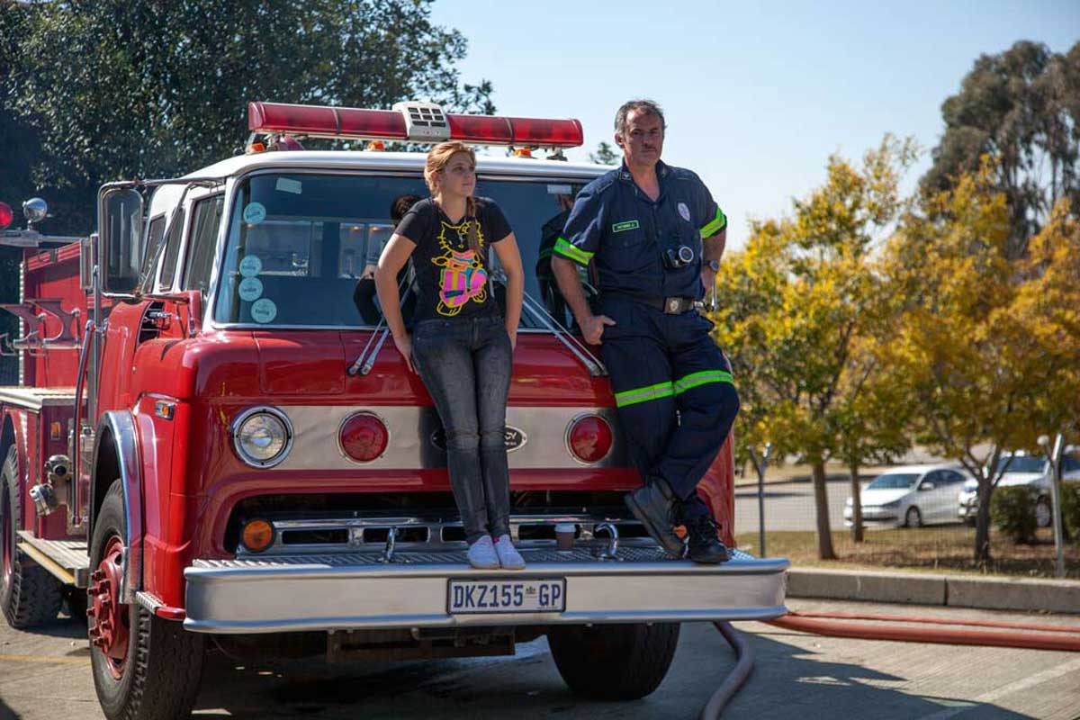 Female and male firefighter sitting on vintage red fire truck at SAESI emergency services competition event Nasrec